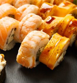 Set of colorful rolls with shrimp, salmon, avocado, cheese on a black stone plate, close-up. Asian cuisine, sushi, seafood.