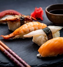 Tasty sushi sashimi set composition with shrimps, ginger and soy sauce served with chopsticks and green wasabi on black round plate. Traditional asian food with rice and seafood